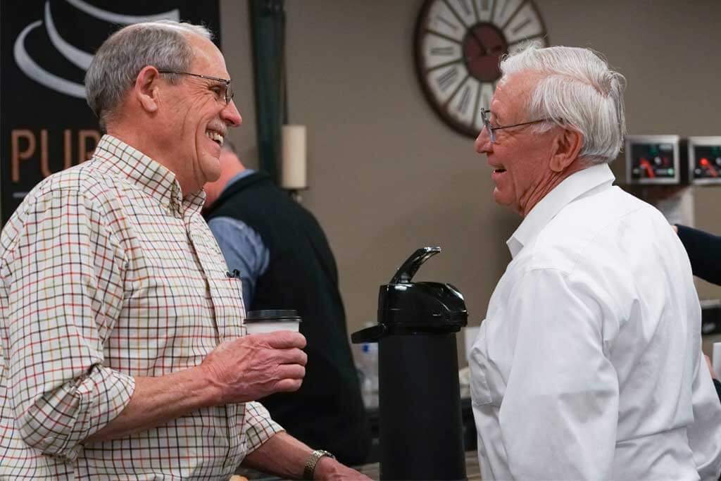 two senior citizens talking while drinking coffee