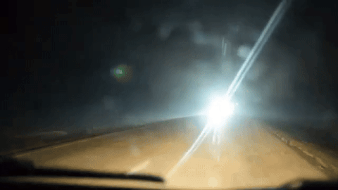 Car driving down highway with bright glare from on coming car shining through windshield.